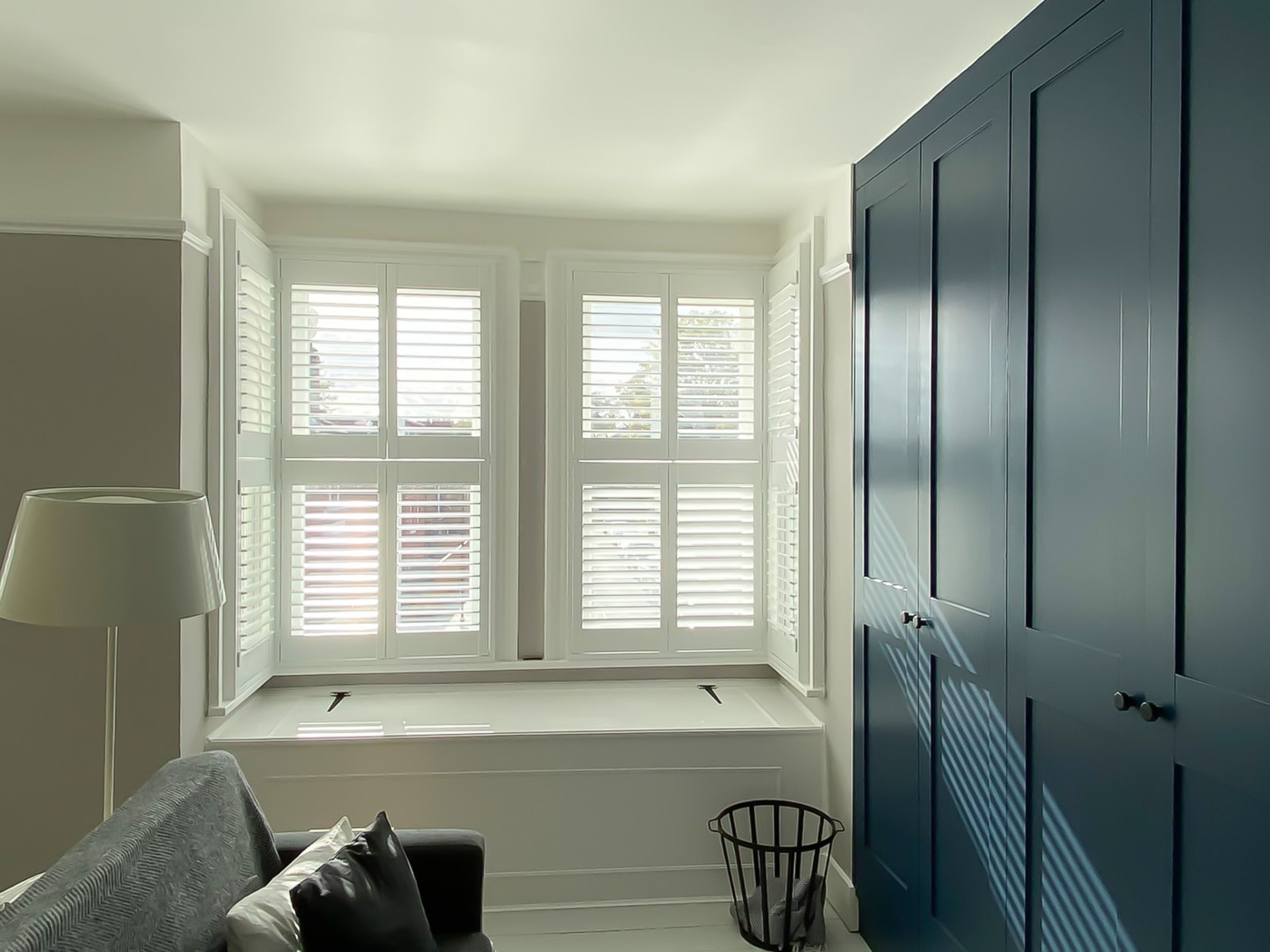 Full-height white shutters in a bedroom bay with window seat