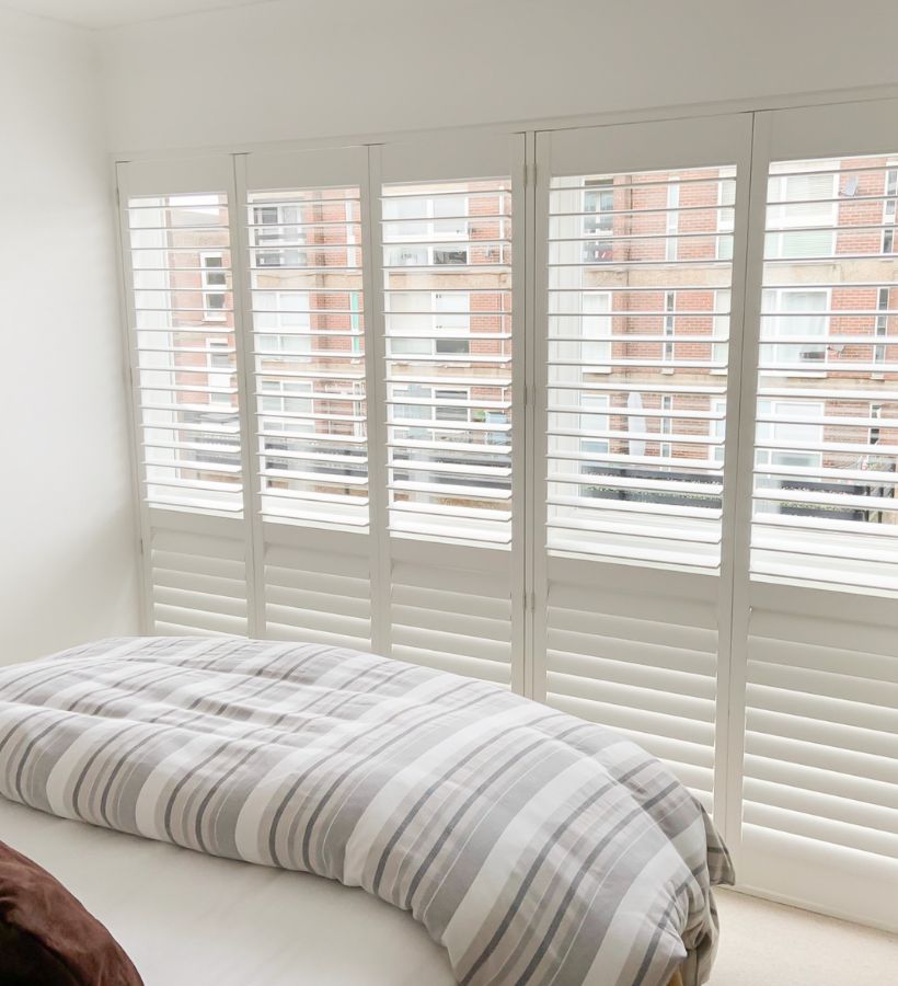 Full-height white plantation shutters in a city-view bedroom