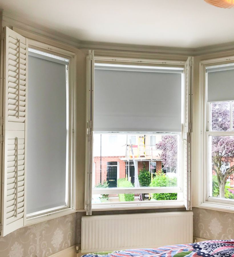 Cream shutters with roller blinds in a period bay window