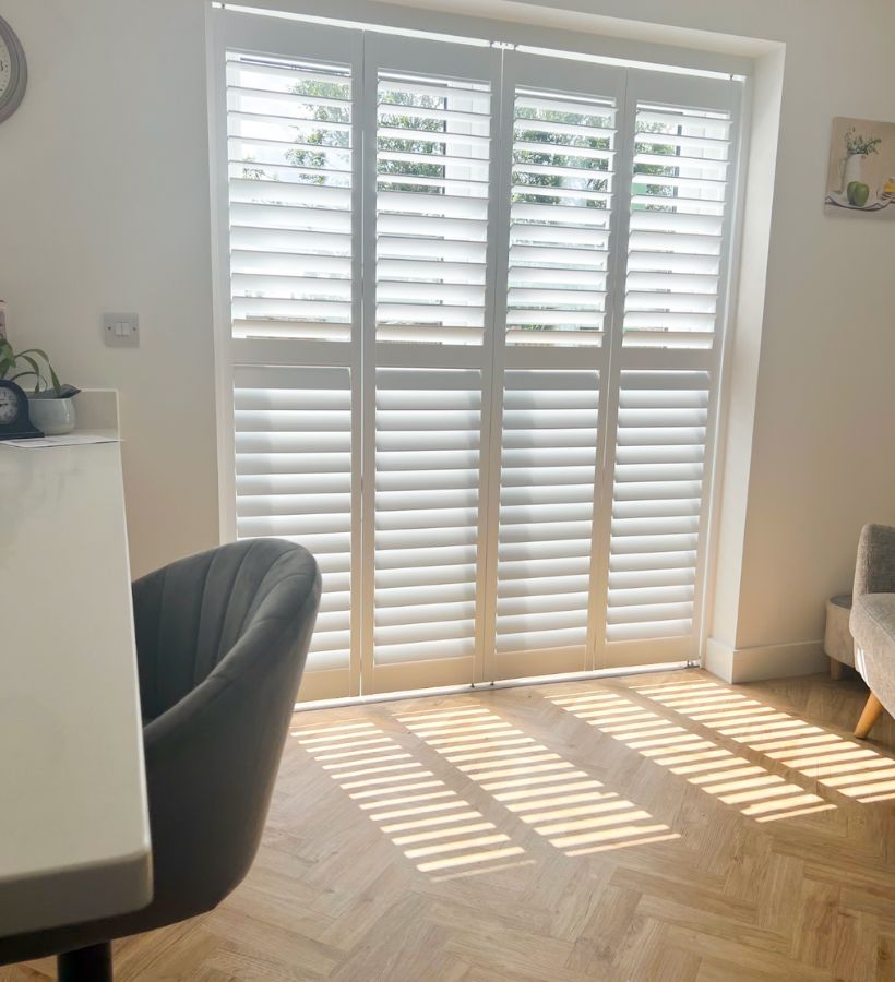 Full-height white shutters on patio doors casting striped sunlight