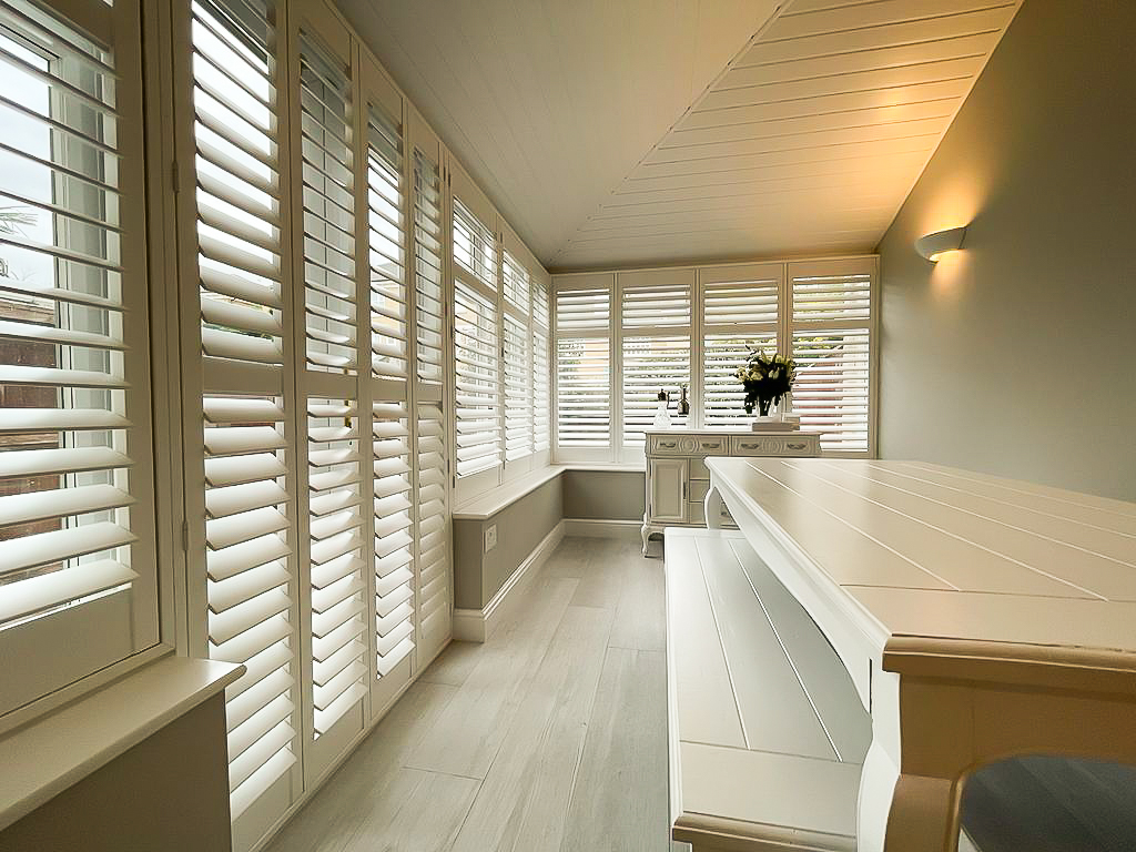 Cream shutters wrapping a garden room with bench seating